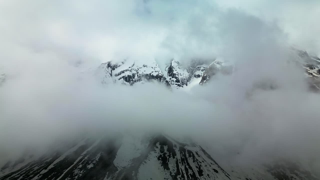 Thick clouds drifting around snow-covered mountains of the Annapurna Massif in Nepal, revealing glimpses of dramatic high-altitude peaks and rugged terrain of the Himalayan range