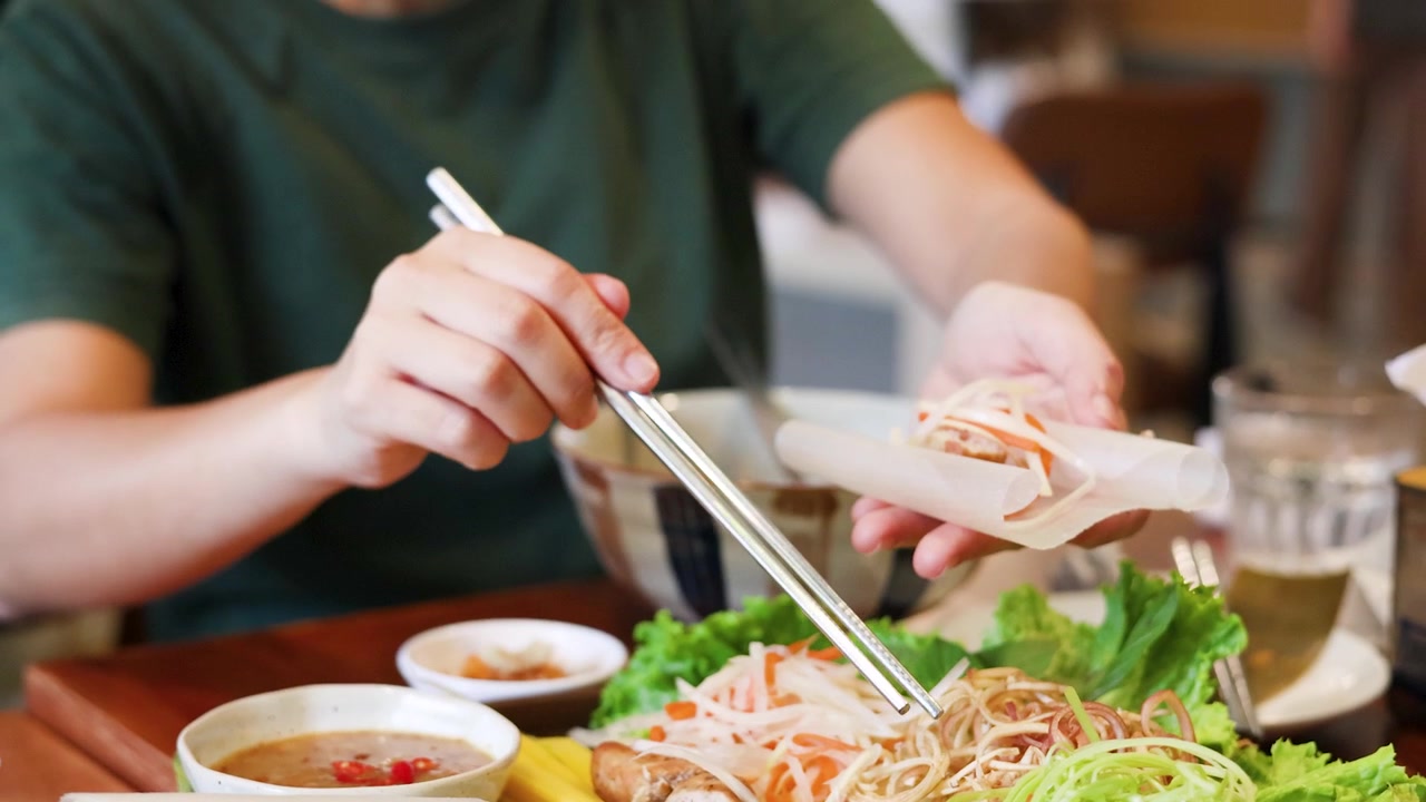 Một người phụ nữ mặc áo xanh lá cây dùng đũa để cuốn những cuốn gỏi cuốn tươi Việt Nam.