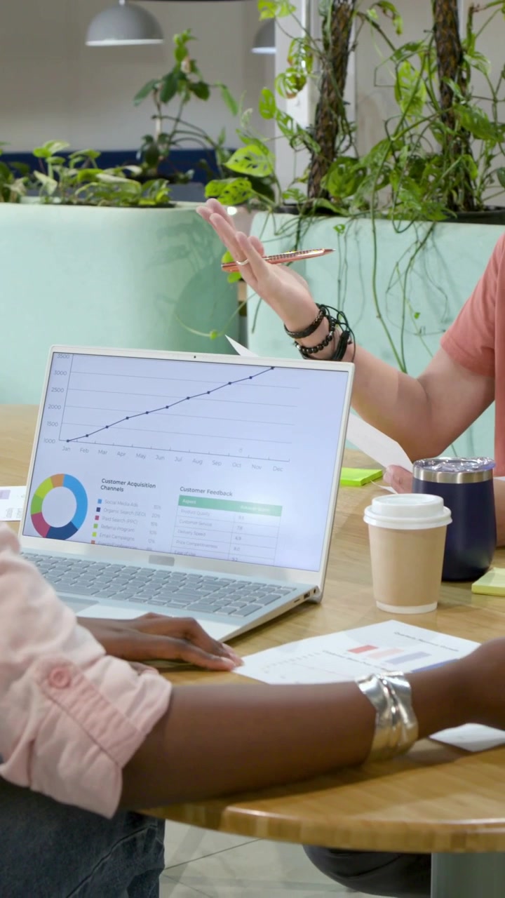 Vertical video: Sparking laptop chart, two coworkers gesturing, writing, analyzing data in office