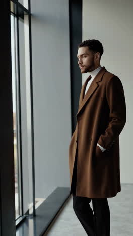 stylish man in brown coat posing by a window