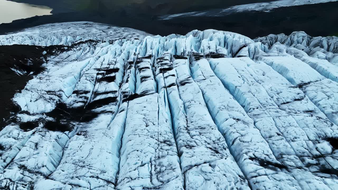 Close aerial sweep over a fractured Icelandic glacier, revealing deep crevasses, dark volcanic streaks, and dramatic frozen textures carved by shifting ice and rugged arctic forces