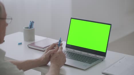 el hombre jubilado se está comunicando en línea usando una computadora portátil con chat de video, pantalla verde en la pc para la postproducción