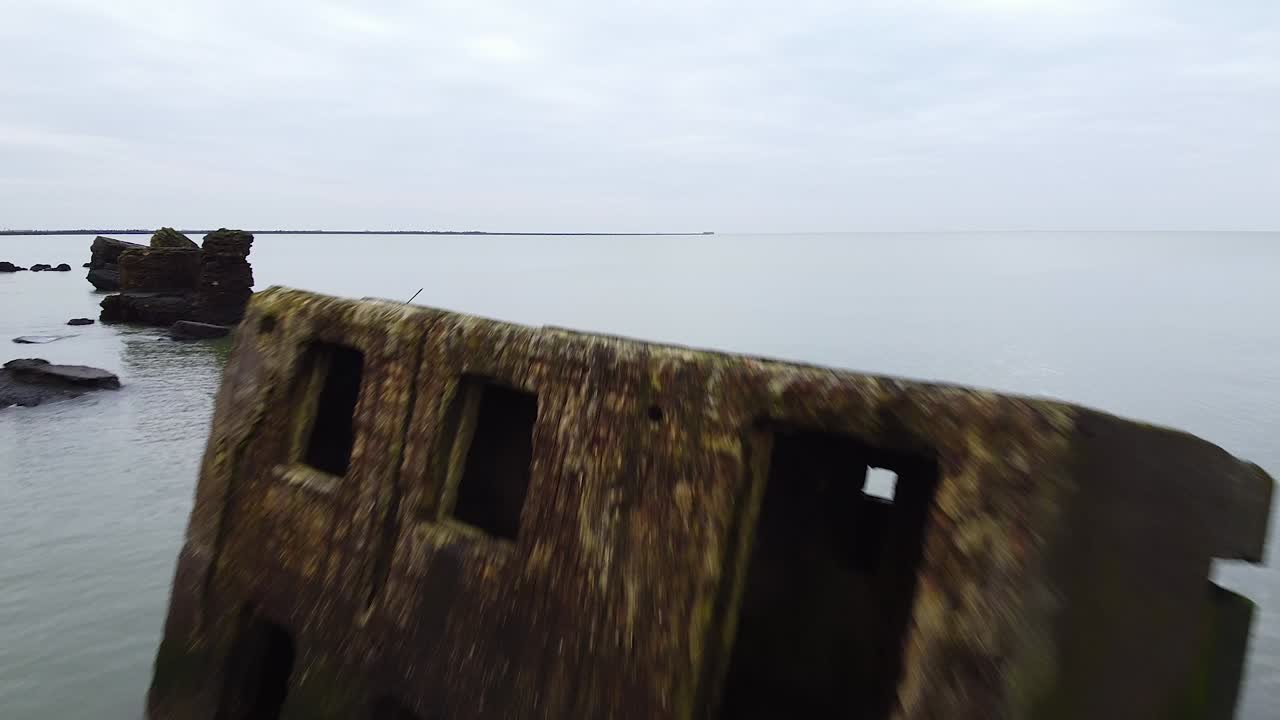 Aerial view of abandoned seaside fortification bunker in water at Karosta Northern Forts on the beach of Baltic sea in Liepaja in overcast spring day, low altitude ascending drone shot moving forward