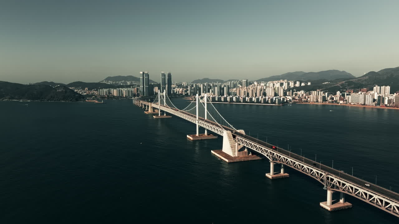 Aerial View of a Suspension Bridge over the Ocean, with Cityscape in the Background