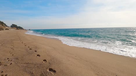 Hermosa-Playa-De-Arena-Mediterránea,-Maresme-Barcelona,-San-Pol-De-Mar,-Con-Rocas-Y-Mar-Tranquilo-Y-Turquesa-Con-Huellas-En-La-Arena