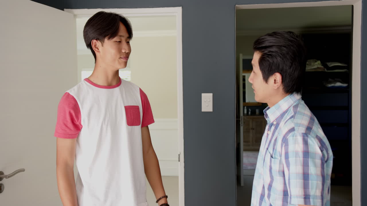 Asian father and teenage son smiling and talking at home