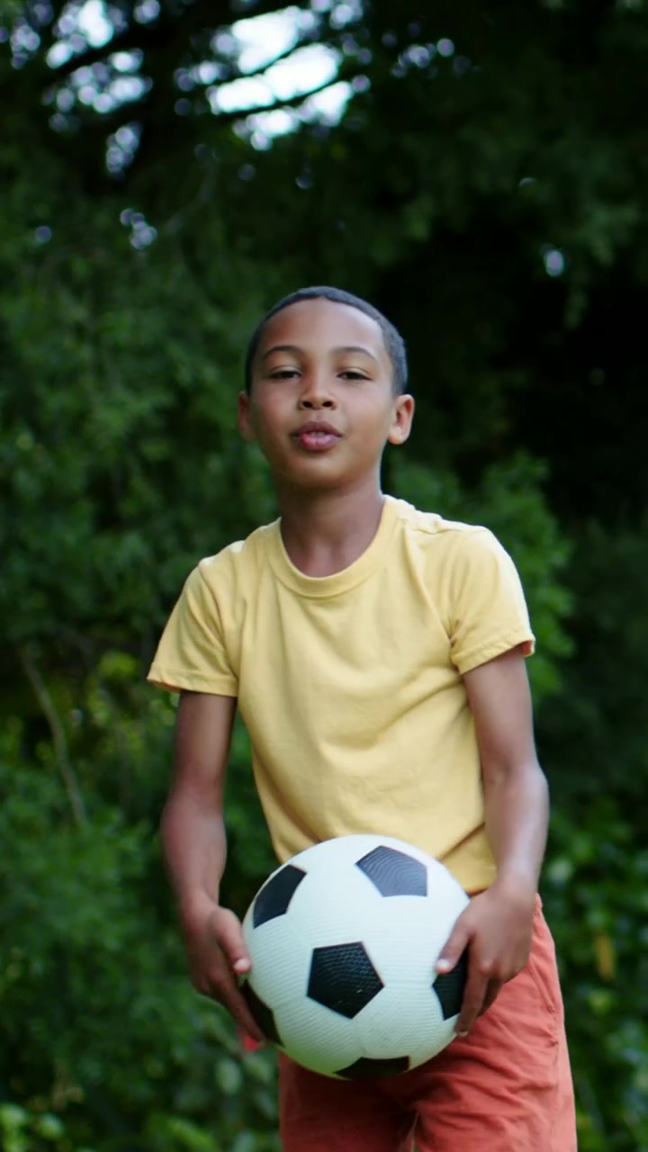 Vídeo vertical: Criança com camiseta amarela pegando bola de futebol, jogando e pegando no jardim, treinando.