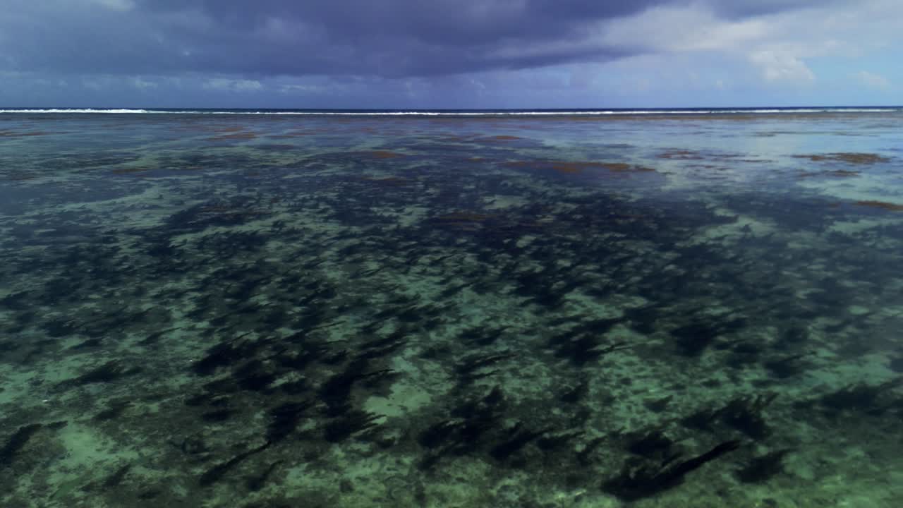 Shallow reef waters at St. Felix Beach in Mauritius under a moody sky, with waves approaching, raw nature, coastal tension, and oceanic transition.