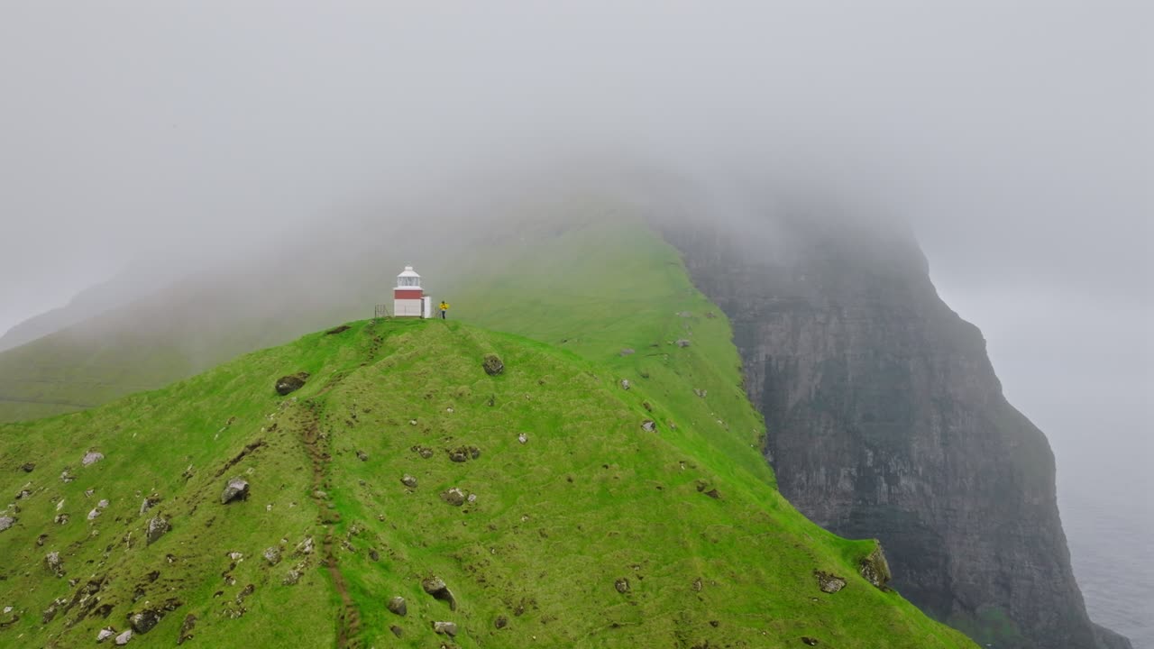 A remote lighthouse surrounded by green cliffs and fog in the Faroe Islands, Kallur Lighthouse