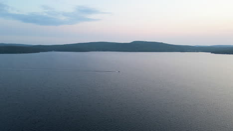 Aerial shot of boat racing towards tree covered coastline and sunset with thick green tree covered mountains in background. Calabogie Ontario