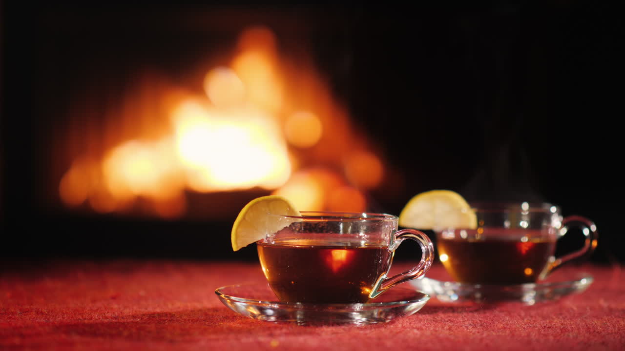 화로에 불이 타오르는 배경에 빨간 식탁보가 있는 탁자 위에 뜨거운 차 두 컵