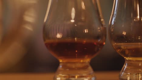 two whisky glasses with amber liquid sit on a wooden table, softly illuminated by warm candlelight. gentle camera movement creates a dreamy, intimate atmosphere