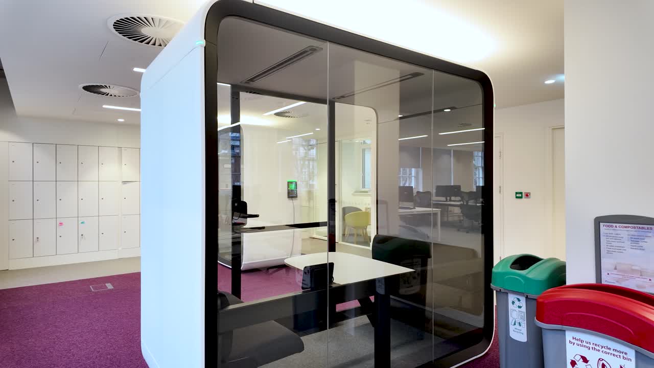 Futuristic glass walled office pod provides a quiet workspace for focused work and important calls in a shared office environment