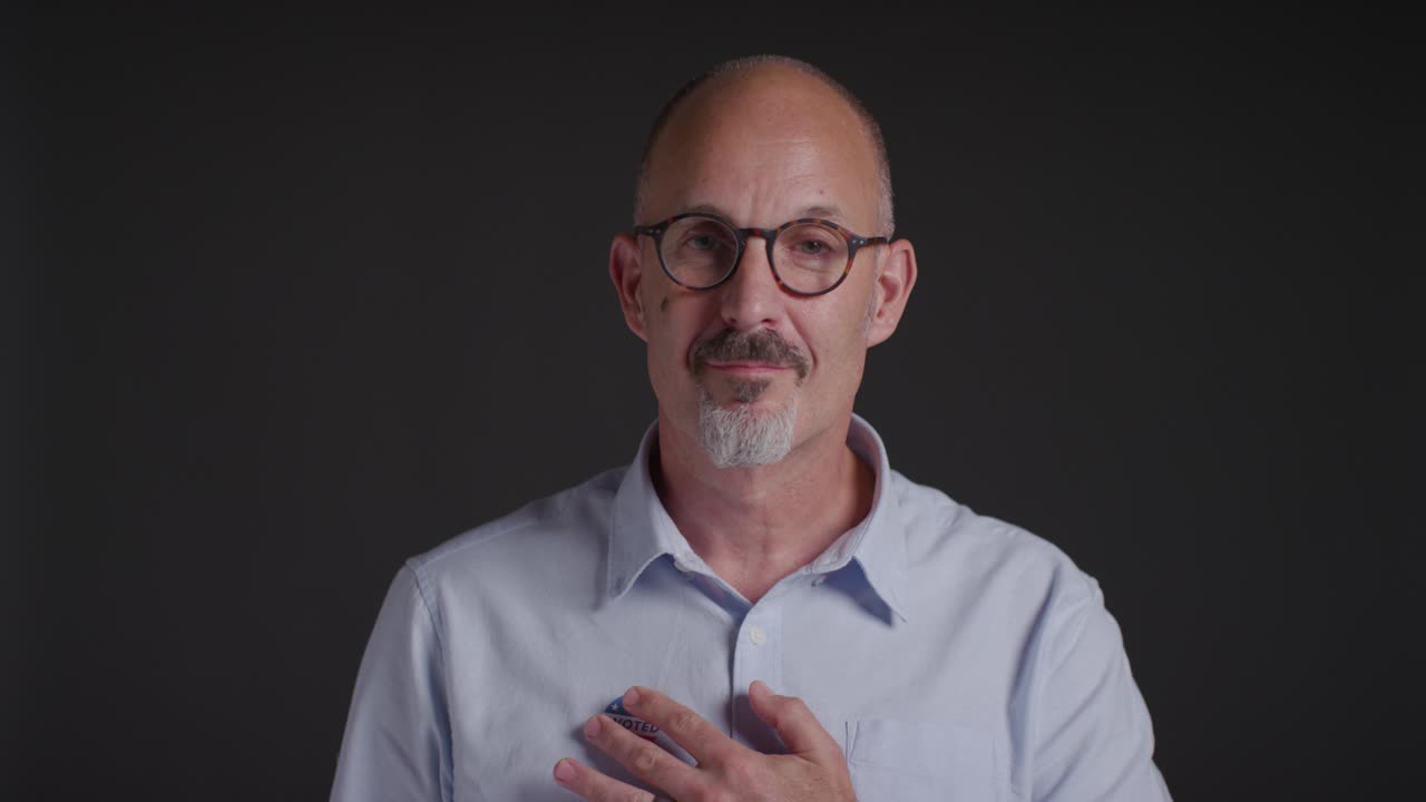 Studio Portrait Of Mature Man Putting I Voted Sticker On Shirt In American Election