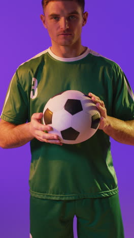 video vertical del retrato de un jugador de fútbol masculino caucásico con una pelota de fútbol sobre iluminación rosa neón