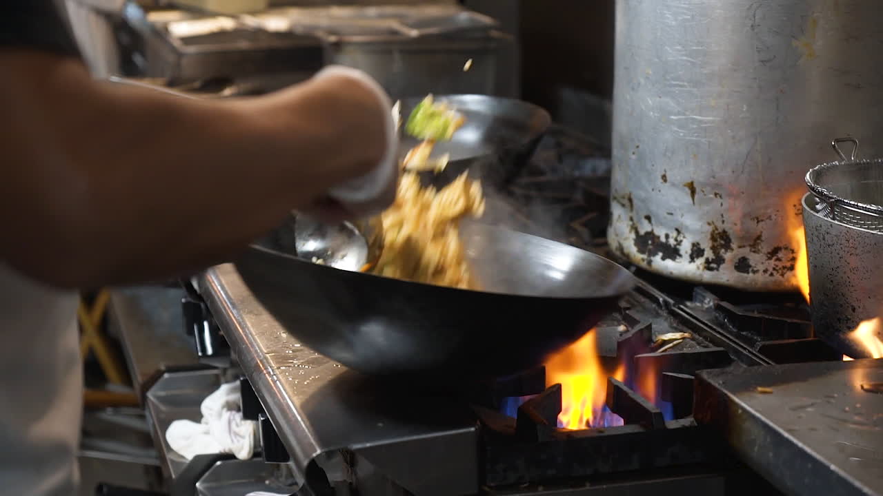 Lo chef salta e mescola riso fritto nel wok su fiamma viva sul fornello commerciale in una cucina di ristorante, slowmotion HD