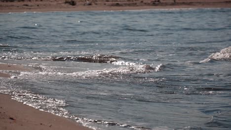 Waves-of-blue-ocean-water-hitting-a-sand-beach-on-slow-motion