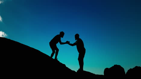 silhouettes of two people reaching the mountain top