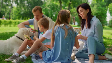 little boy feeding labrador on picnic. cheerful family rest on green grass.
