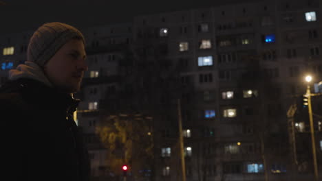 Low-angle-looking-up-tracks-man-in-jacket-and-beanie-walking-through-urban-city-on-frigid-cold-night