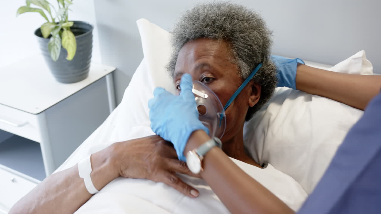 Dottoressa afroamericana che applica una maschera d'ossigeno a una donna anziana in una stanza d'ospedale, al rallentatore