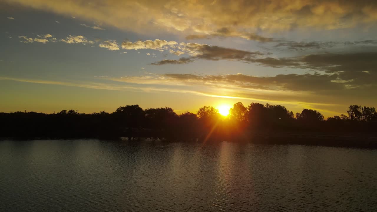 imágenes aéreas dinámicas de una puesta de sol con resplandores de sol corriendo a través de los árboles mientras volaba sobre un río en la ciudad de córdoba, argentina.