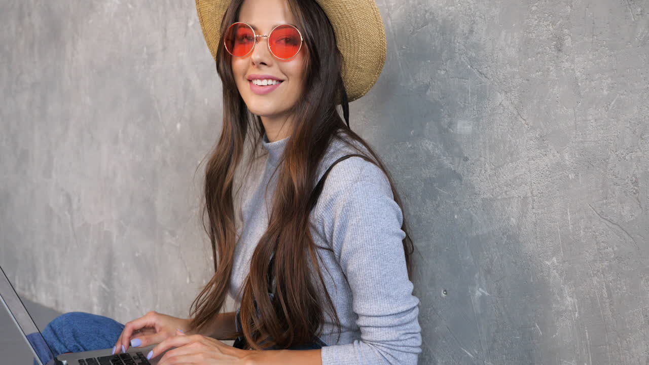 mujer trabajando en una computadora portátil, estilo casual, fondo de hormigón