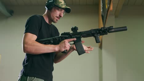 un hombre con gafas de protección y protección de oídos descarga un arma larga quitando el clip de la revista y comprobando si hay balas en la cámara en un campo de tiro interior