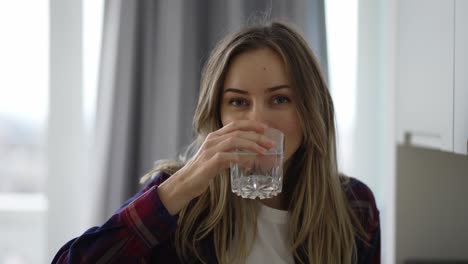 Mujer-Bebiendo-Agua-En-La-Cocina-Doméstica,-Mirando-A-La-Cámara