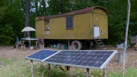 old metal camper trailer in woodland scene with off-grid solar panels pan up