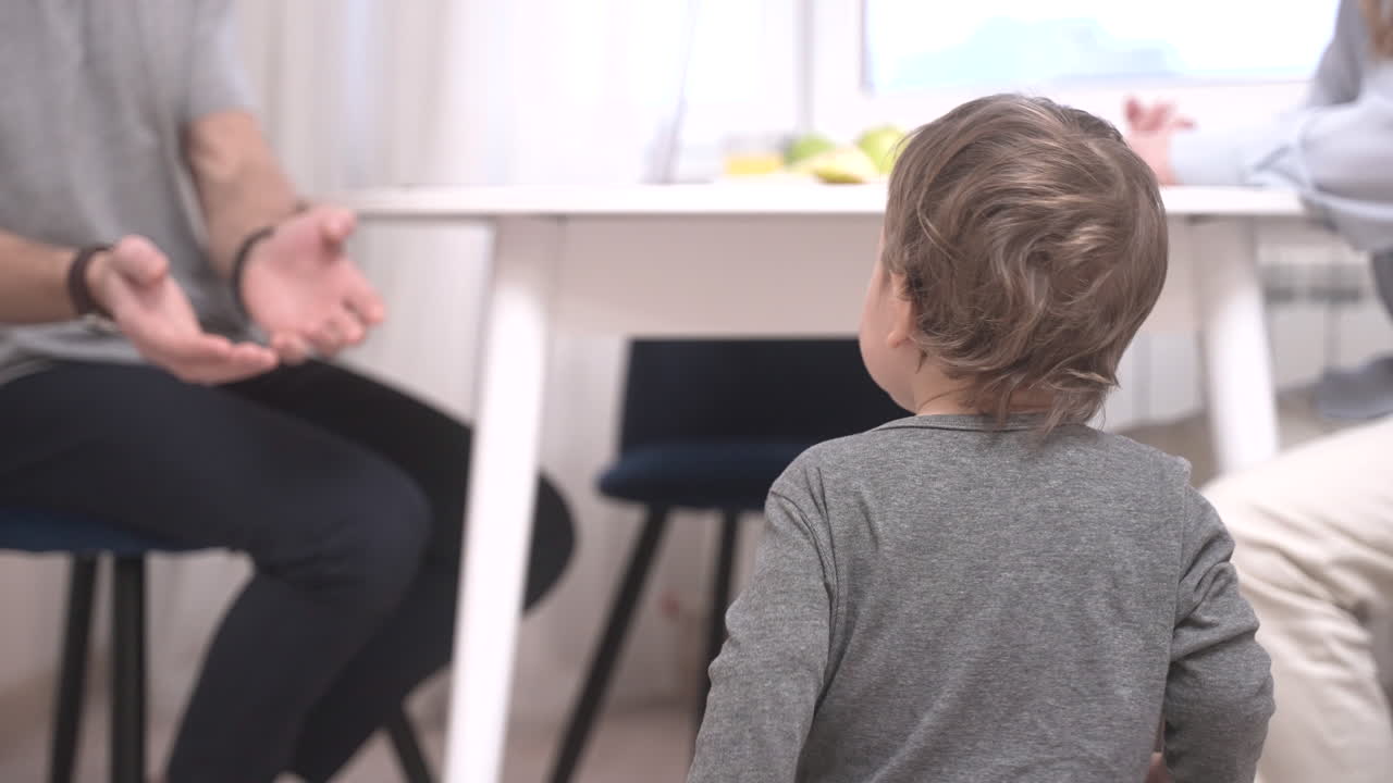 Genitori seduti a un tavolo e il loro bambino è vicino a loro sul pavimento 1