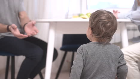 parents sitting at a table and their baby is near them on the floor 1