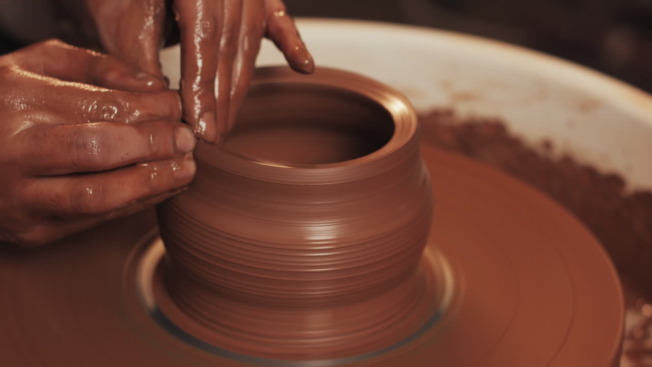 primer plano de manos moldeando arcilla en una rueda de cerámica