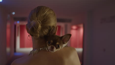 woman carrying chihuahua on her shoulder in a hotel corridor at night