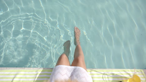 Low-section-of-biracial-teenage-girl-sitting-with-legs-in-sunny-pool,-copy-space,-slow-motion