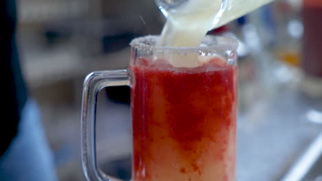 bartender pours frozen margarita over strawberry puree in beer mug, slow motion hd