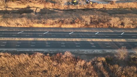 An-aerial-view-of-a-salt-marsh-next-to-a-multilane-road-with-a-few-cars-driving-by,-shot-on-a-sunny-day