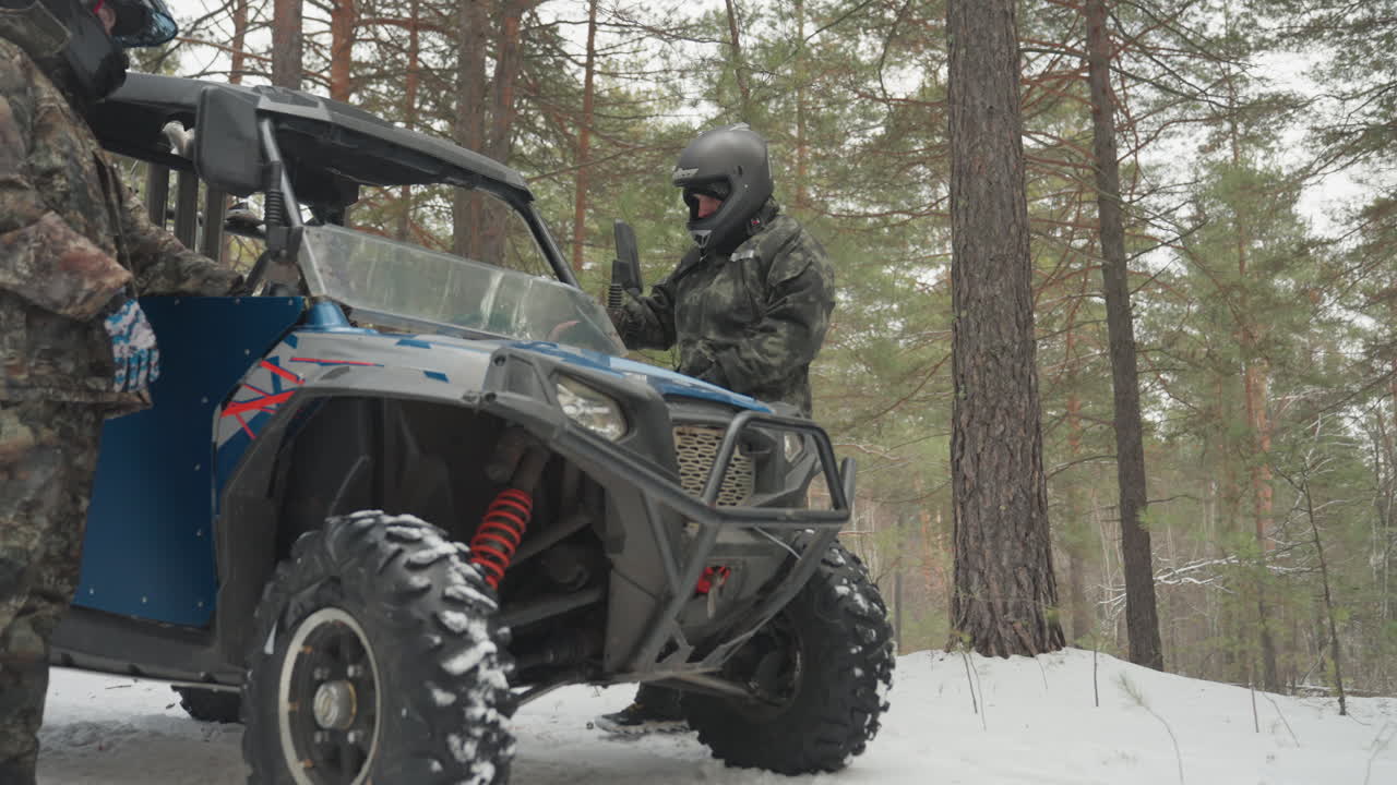 I piloti si equipaggiano con entusiasmo. Esploratori entusiasti pronti a conquistare impervi sentieri di montagna. Avventurieri in mimetica e con casco si preparano per un'estrema spedizione fuoristrada attraverso la natura selvaggia invernale.