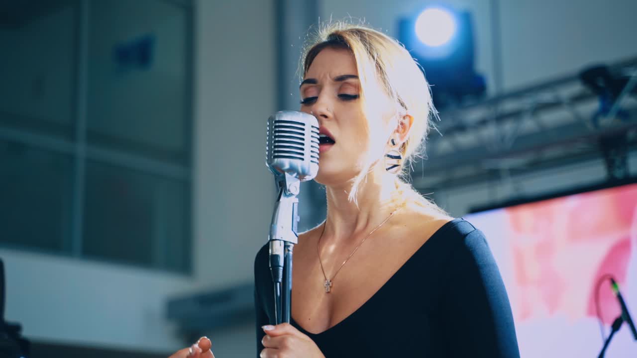 Blonde woman sings into the microphone. Attractive singer standing on the stage and singing a song. Musical entertainment.