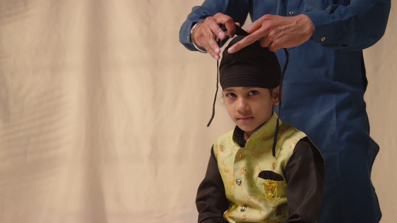 fotografía de estudio de un padre atando un turbante a la cabeza de un joven sikh que lleva un chaleco tradicional como secuencia parte 5 de 10