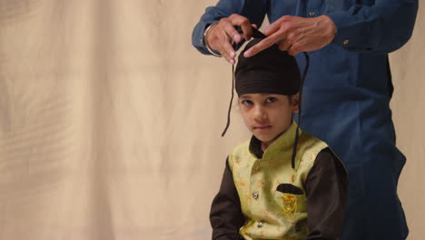 Foto-De-Estudio-De-Un-Padre-Atando-Un-Turbante-En-La-Cabeza-De-Su-Hijo-Sikh-Que-Lleva-Un-Chaleco-Tradicional,-Como-Se-Muestra-En-La-Secuencia,-Parte-5-De-10