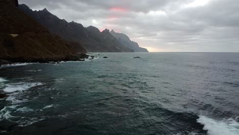 Beautiful-coast-with-view-to-the-ocean-and-mountains.-Morning-dusk,-high-aerial-view-on-hectic-coast-waves.-Brown-high-hills-on