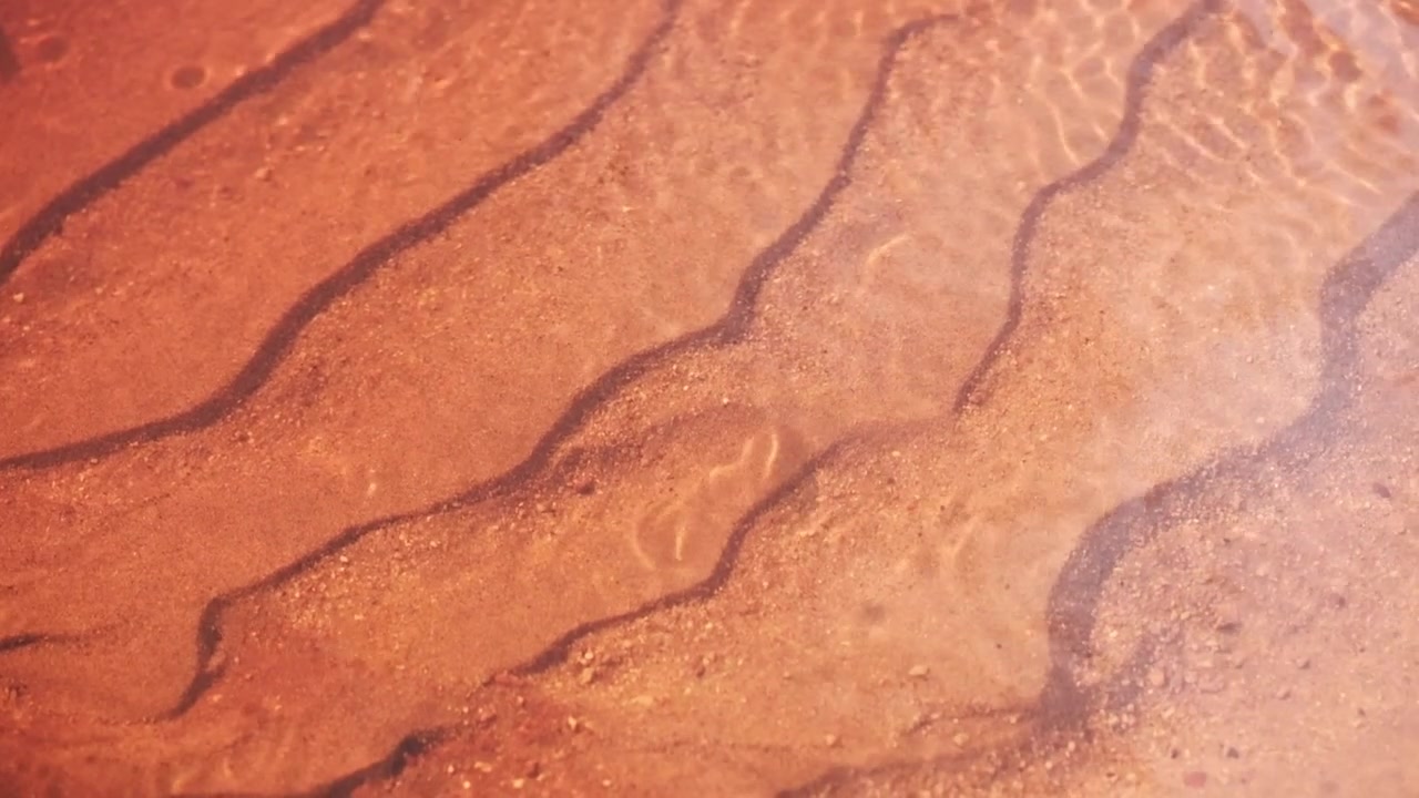 Sabbia di fiume sotto la superficie di un ruscello che scorre dolcemente.