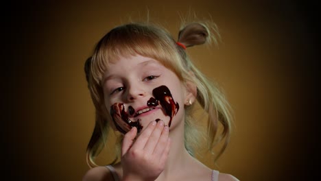 portrait of teen smiling child kid girl smears face with melted chocolate and showing thumbs up sign