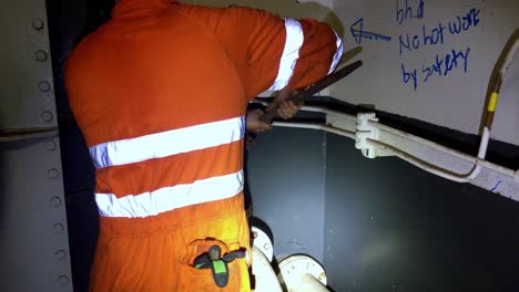 Boat-technician-using-a-wrench-to-open-fuel-oil-tank-wearing-an-orange-jumpsuit