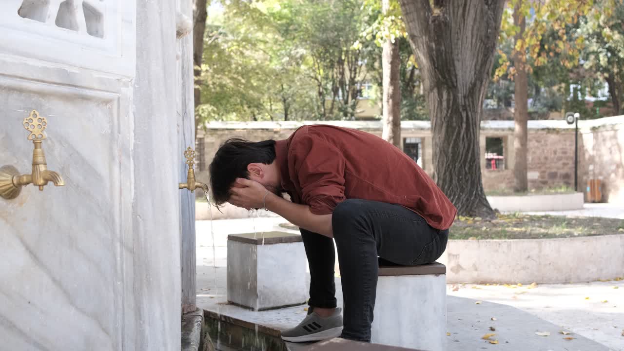 Side view of a Muslim bearded man performing ablution, a man washing his hand and face in a mosque fountain