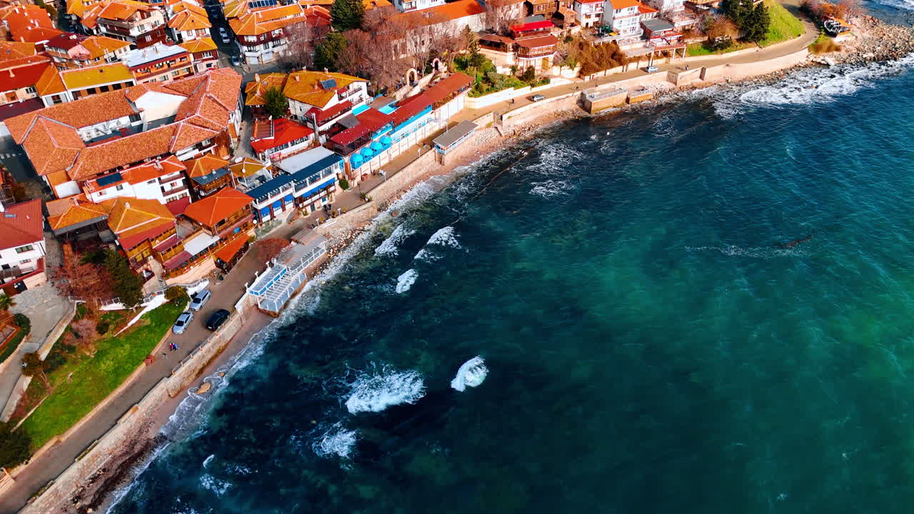 Vista aerea di una città costiera con tetti rossi e mare. Ripresa diagonale con drone di una strada costiera e di edifici tradizionali che si affacciano su un mare cristallino con rocce sottomarine.