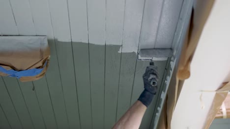 applying white latex paint to the wooden ceiling of a house using a paint roller brush - low angle shot