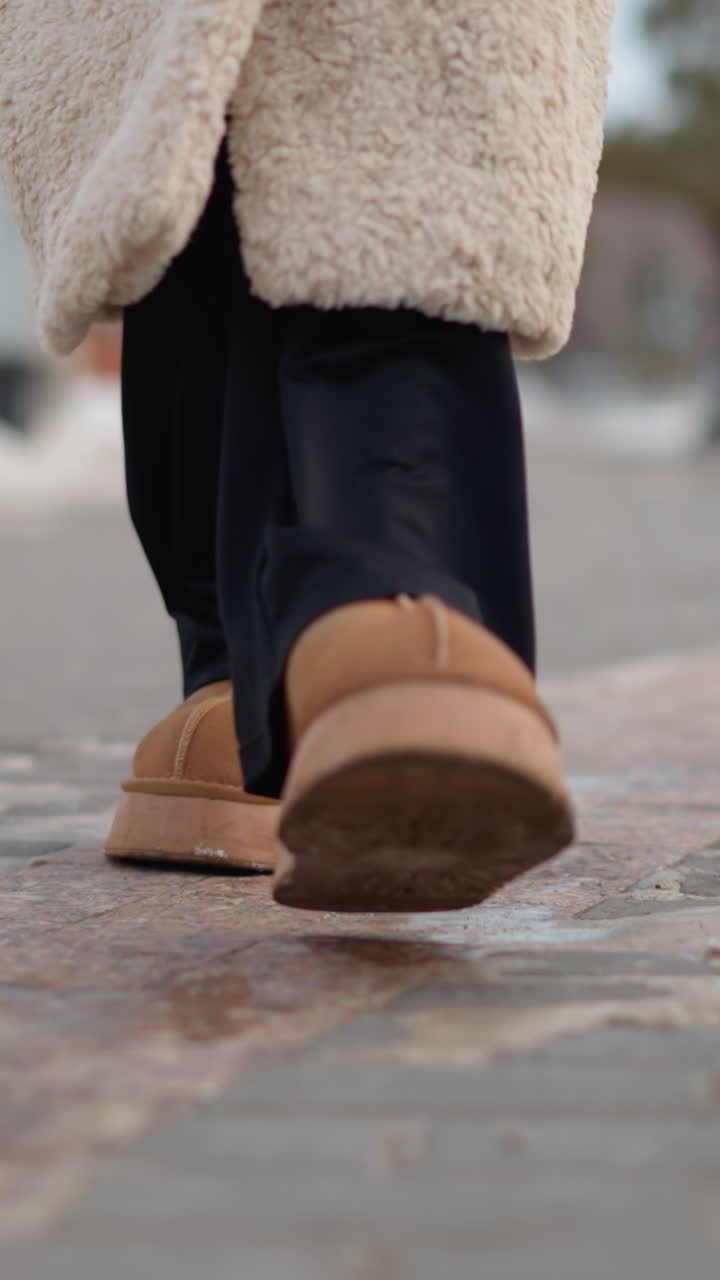 adolescente blanco caminando por la acera con botas color canela y abrigo de borreguito, paso firme sobre la acera helada, con el dobladillo del abrigo y los pantalones negros visibles, recado o trayecto urbano, ritmo concentrado y firme