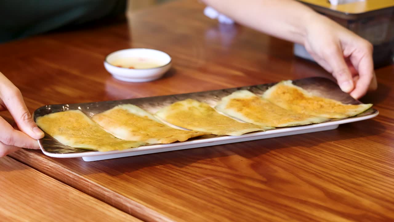 Tangan Menyajikan Sepiring Pangsit Goreng di Meja Kayu